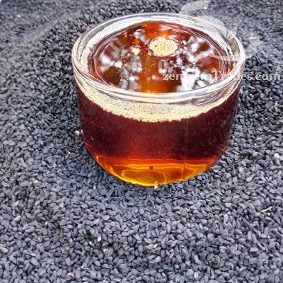 Glass of black cumin oil on Raw seeds